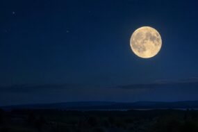 Heller Vollmond am dunkelblauen Nachthimmel über einer stillen Landschaft