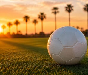 Weißer Fußball ohne Aufdruck auf einem Trainingsplatz bei Sonnenuntergang, im Hintergrund Palmen